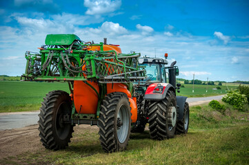 new tractor with trailed sprayer, near winter crop field, spring crop fertilizers, beautiful sky