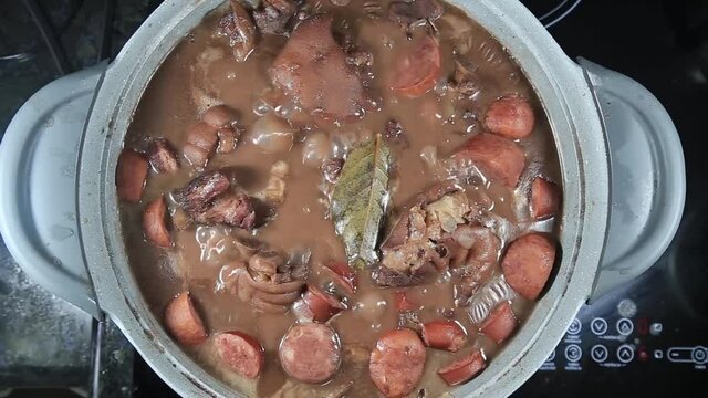 Traditional Brazilian feijoada boiling in the rustic pot in close-up and top view