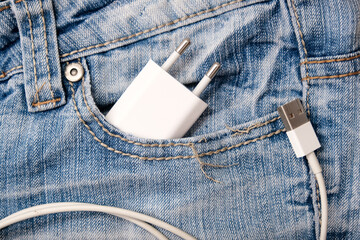 Usb charger, wire adapter for smartphone and gadgets in a jeans pocket taken on a trip