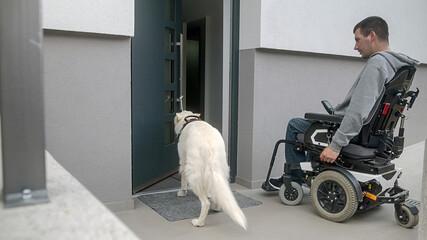 Man on electric wheelchair, and his assistance dog. A service dog closes a home front door by...