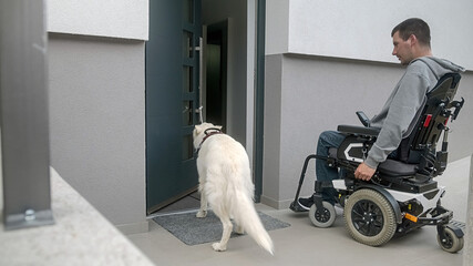 Man on electric wheelchair, and his assistance dog. A service dog closes a home front door by pulling a rope tied to a door pull handle.