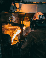 Vertical shot of an adult industrial worker in uniforms melting metal in a factory