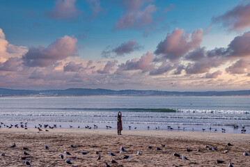 Fototapeta na wymiar Woman stretching her arms on beach admiring seascape while surrounded by seagulls on sand