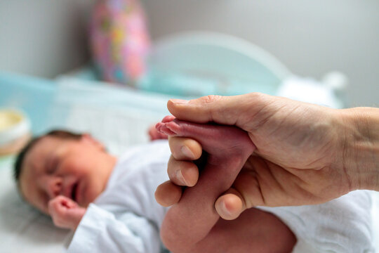 Close-up of father's hand massaging and warming up crying newborn baby's tiny foot during diaper change. New life and family concept