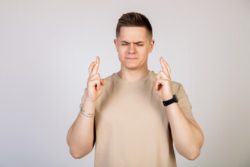 Photo of a young, nervous, excited man with his fingers crossed. Man holding fingers crossed with...
