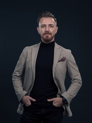 Fototapeta premium Portrait of a stylish elegant senior businessman with a beard and casual business clothes in photo studio isolated on dark background gesturing with hands