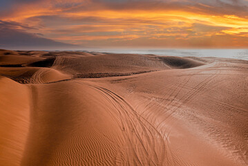 Obraz na płótnie Canvas Beautiful sunset over sand dunes with tyre marks at beach against dramatic sky, Tyre marks on sand at beach