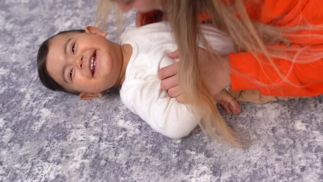 Mother makes her baby laugh. The mother plays with the baby's belly lying on the floor and the baby laughs. This is a Slow motion video.