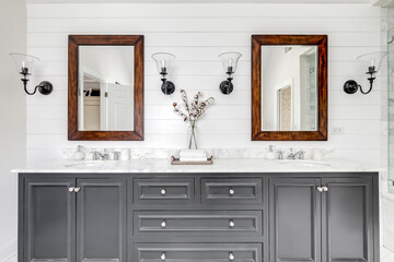A luxurious renovated bathroom with a grey vanity, rustic wood framed mirrors, and chrome faucets and hardware.