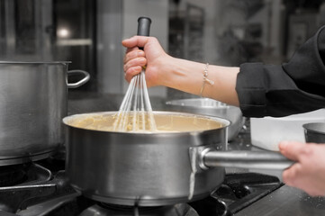 Chef stirring sauce in stainless steel pot, close-up. Professional kitchen, restaurant. High quality photo