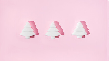 Three geometrical white Christmas trees on pastel pink background. Minimal romantic composition for Christmas or New Year's eve celebration or web banner