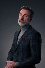 Obraz premium Portrait of a stylish elegant senior businessman with a beard and casual business clothes in photo studio isolated on dark background gesturing with hands
