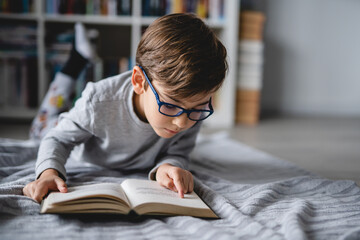 One caucasian boy lying on the floor at home in day reading a book front view copy space real...