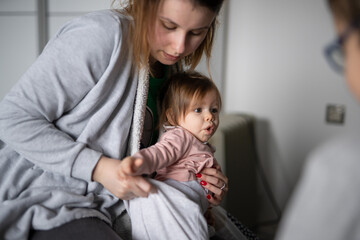 Small caucasian baby getting dressed mother young woman hold her child daughter girl while dressing her at home changing clothes real people family domestic life care and parenthood concept