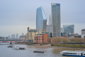 Fototapeta premium UK, London, 11.12.2021:&nbsp;A view of the Thames with ships, tall buildings in the background and a cloudy sky.