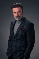 Obraz premium Portrait of a stylish elegant senior businessman with a beard and casual business clothes in photo studio isolated on dark background gesturing with hands