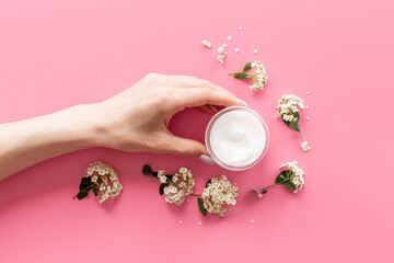 Hand hold white flowers with skin cream in glass jar. Herbal cosmetic