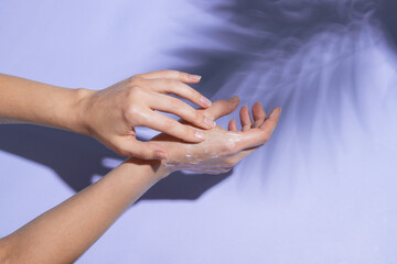 Beautiful female hands in sunlight apply cream on very peri background with shadow of palm leaves