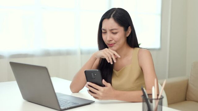 Young asian woman using smartphone chatting video conference online sitting in living room at home. Business Woman looking at screen Meeting on social media. Work from home.