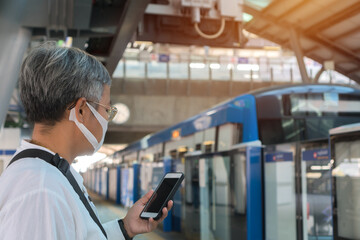 Asian Tourists travelers use smartphone checking metro subway train at station with wearing face...