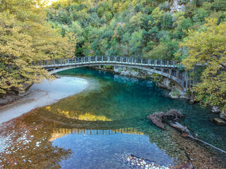 Fototapeta na wymiar Scenic view over the natural beauty at the famous voidomatis river passing from the National park of Vikos and a beautiful bridge near Aristi village in Autumn. Epirus, Greece, Europe
