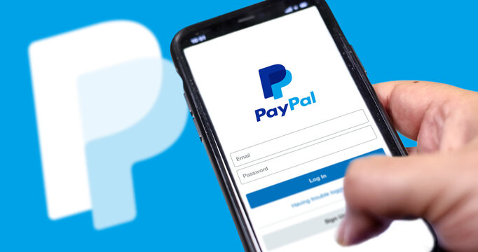 Hand holding a smart phone with Paypal app login page on screen