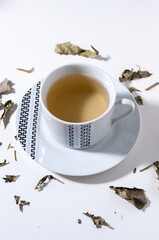 A cup of "espinheira santa" (Maytenus ilicifolia) tea on white table with a few leaves . This tea is commonly prescribed for gastric problems.