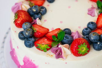 Delicate cake garnished with fresh strawberries blueberries on a pink plain background. Festive dessert with berries