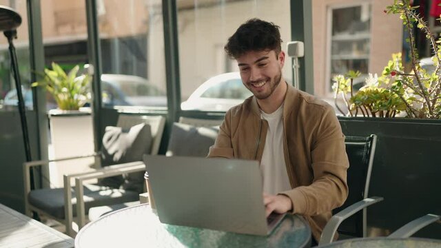 Young hispanic man smiling confident using laptop at coffee shop terrace