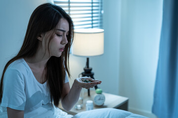 Asian unhappy sick girl in pajamas take medicine before sleep on bed.