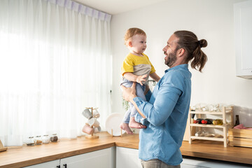 Caucasian loving father tosses cute baby boy child up in living room.
