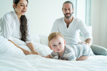 Obraz premium Caucasian parents playing with cute baby boy child on bed in bedroom. 