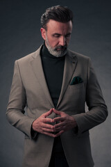 Portrait of a stylish elegant senior businessman with a beard and casual business clothes in photo studio isolated on dark background gesturing with hands