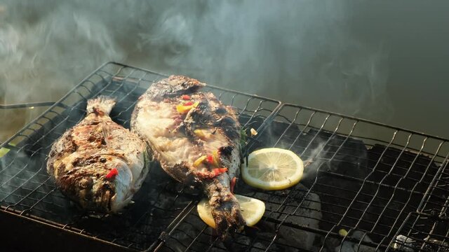 Sea bass or grouper fish grilled over charcoal. Close-up shot cooking seafish with aromatic spices on barbecue grill plate. Baking roasting marinated delicious seafood. BBQ  in summer garden outdoors 