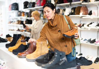 woman selecting boots while standing in salesroom of shoeshop. Old lay making purchases in...