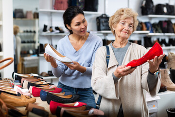 Fototapeta na wymiar Senior woman standing in salesroom of shoeshop and choosing moccasins. woman worker helping her to choose.