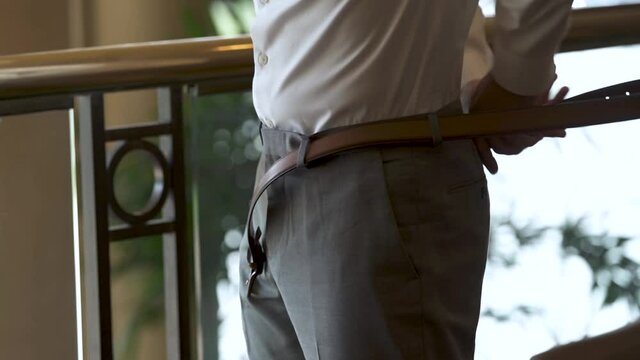 A groom at his wedding putting on his belt to prepare for the wedding ceremony.