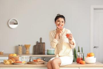 Young woman drinking fresh homemade citrus juice in kitchen