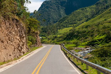Road between tree-filled mountains and a river at the edge in a Colombian landscape.