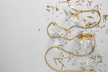 Champagne glasses with golden confetti and beads on white background