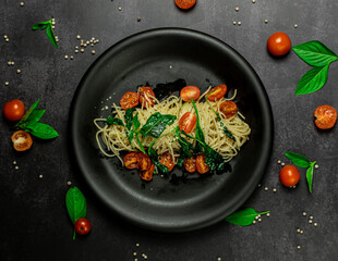 Tasty roasted garlic, seared tomato and wilted spinach pasta. Classic homemade italian spaghetti pasta.  Presented with copy space, top view on dark table.