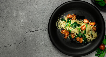 Tasty roasted garlic, seared tomato and wilted spinach pasta. Classic homemade italian spaghetti pasta.  Presented with copy space, top view on gray stone table.