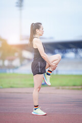 A mature beautiful Asian woman in sports outfits stretching before workout outdoor in the city stadium park in the morning to get a healthy lifestyle. Healthy young woman warming up outdoors