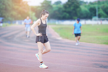 Obraz premium A mature beautiful Asian woman in sports outfits stretching before workout outdoor in the city stadium park in the morning to get a healthy lifestyle. Healthy young woman warming up outdoors