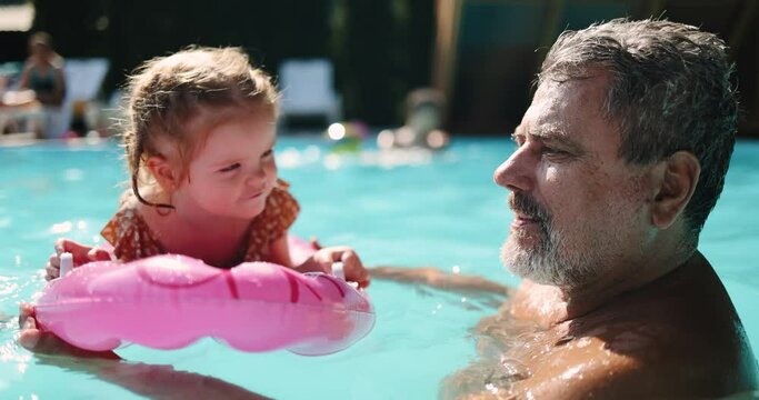 grandpa swimming in a pool together with his granddaughter on an inflatable board. family having fun on summer vacation