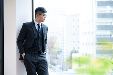 A businessman in a suit smiles as he looks out from a building that looks like a success.