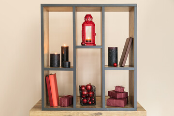 Wooden shelf unit with lantern, burning candles, Christmas gifts and decorations near color wall
