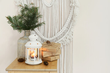 Beautiful lantern with burning candle, Christmas gifts and fir branches on table against color wall