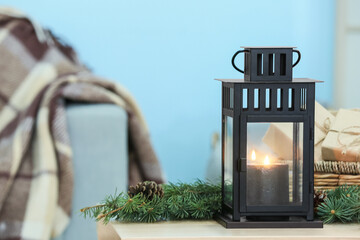 Lantern with burning candle and fir branches on table against color background