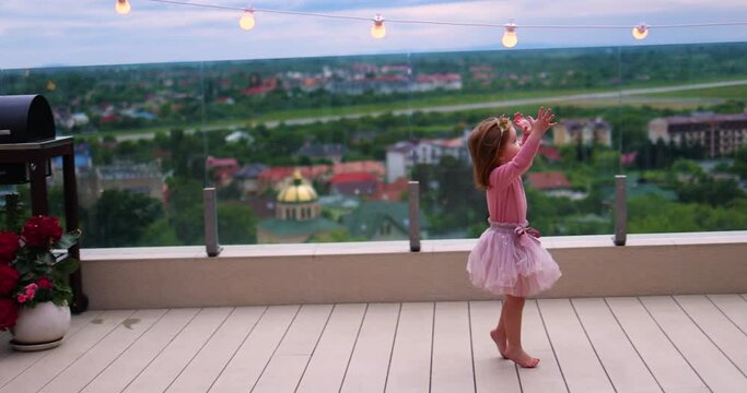 toddler baby girl having fun, running and jumping on rooftop patio at home in the summer evening